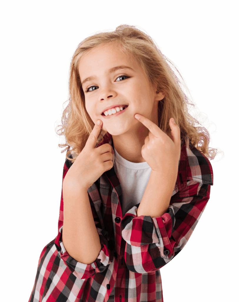 A young girl with curly blonde hair is smiling and pointing to her teeth. She is wearing a red and black plaid shirt over a white t-shirt, against a plain background. Her expression is cheerful and playful.