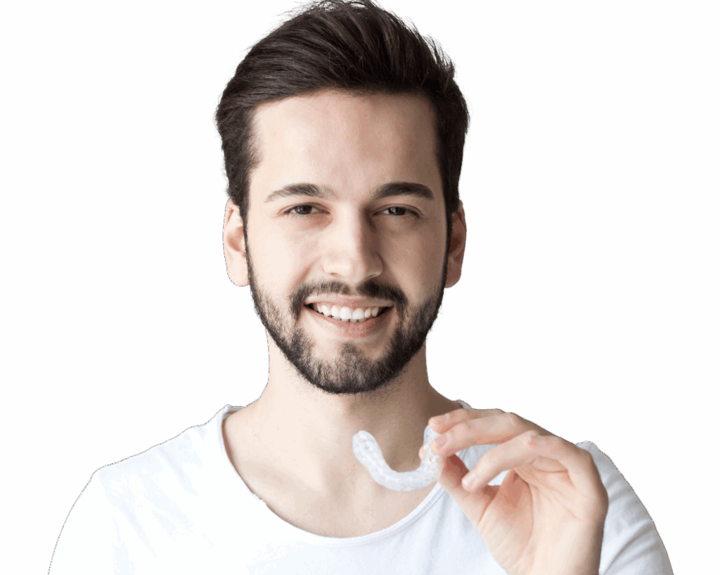 A young man with a short beard smiles while holding an invisible aligner in his hand. He is wearing a plain white t-shirt, and the background is plain, focusing on the subject.