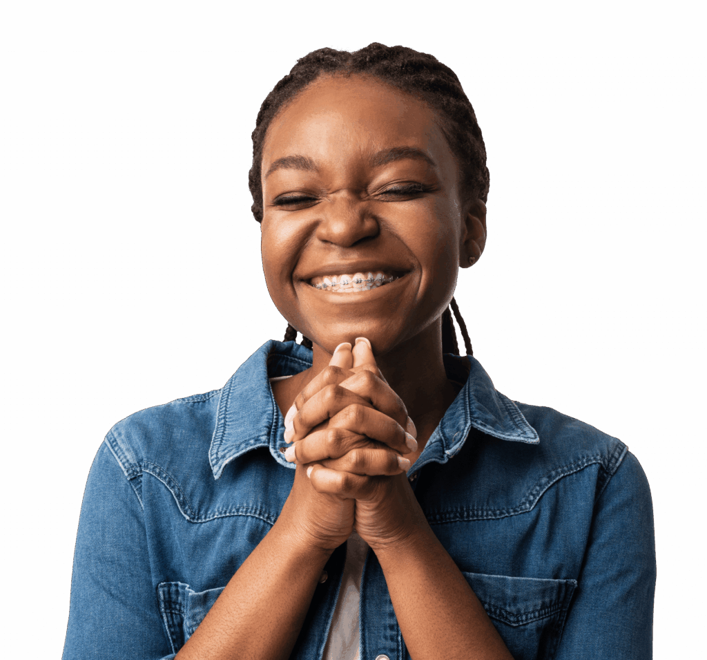 A young girl with braided hair smiles broadly, her hands clasped together in front of her chest. She wears a blue denim jacket over a white shirt, set against a plain background.